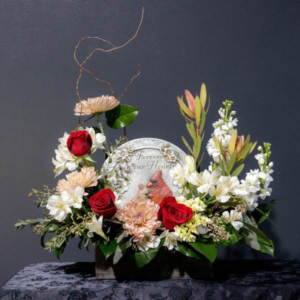 Sympathy floral arrangement with red roses and white blooms around a memorial plaque