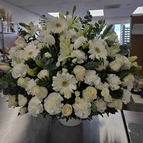 Large white floral arrangement in a round vase with roses, lilies, and daisies