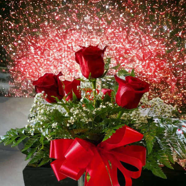 Red roses in a glass vase with a red ribbon and heart confetti