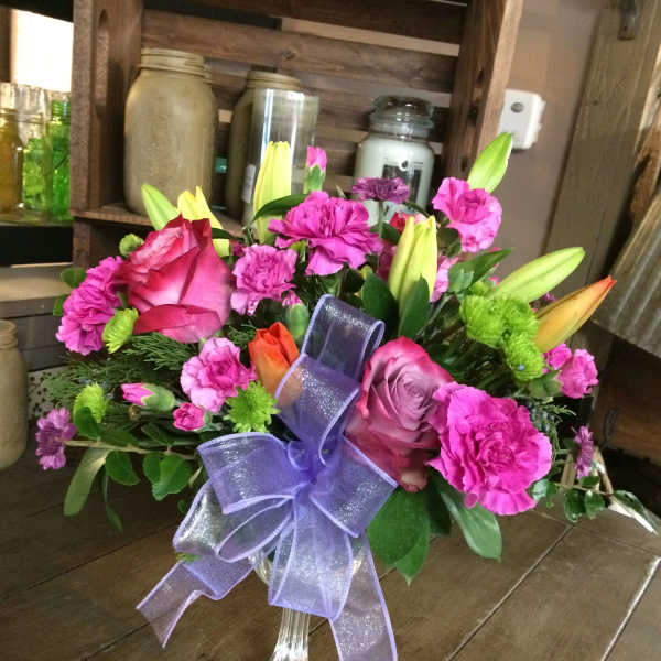 Pink and purple flower arrangement in a clear vase with a lavender ribbon