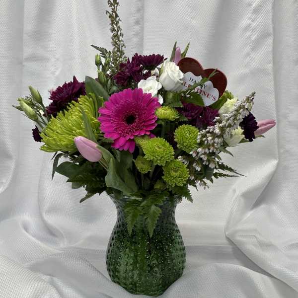 Mixed bouquet in a green glass vase with pink, white, and green blooms