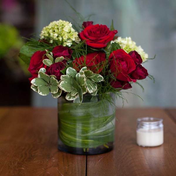 Red roses and pale green blooms in a glass vase on a table