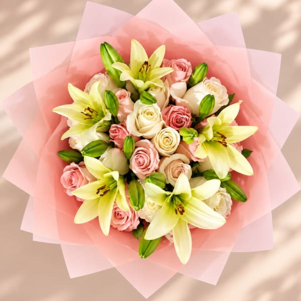 Pink and cream rose bouquet with yellow lilies wrapped in pink paper