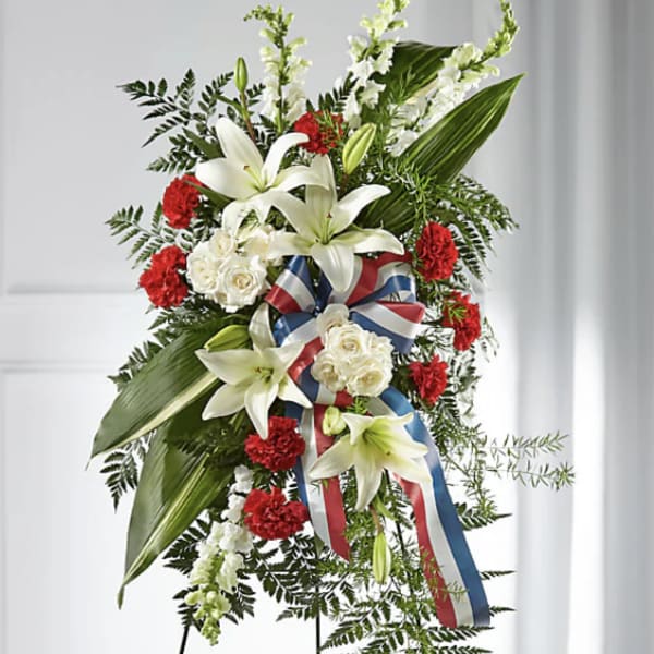 Standing floral spray with white lilies, red carnations, and a ribbon on an easel
