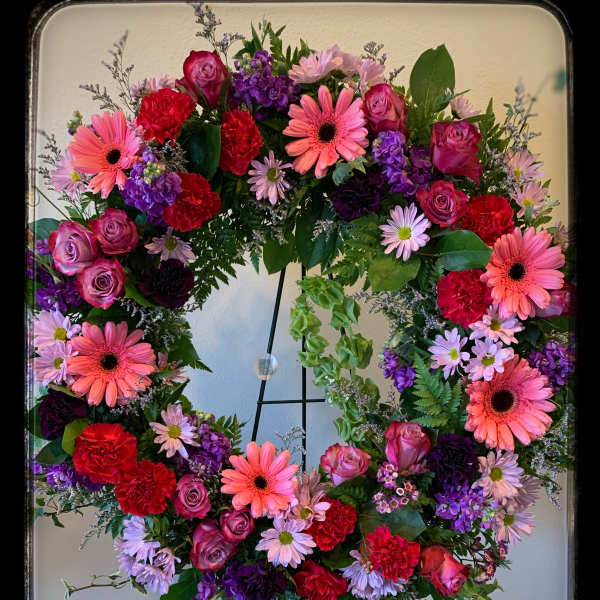 Large floral wreath with pink, purple, and red blooms on a stand