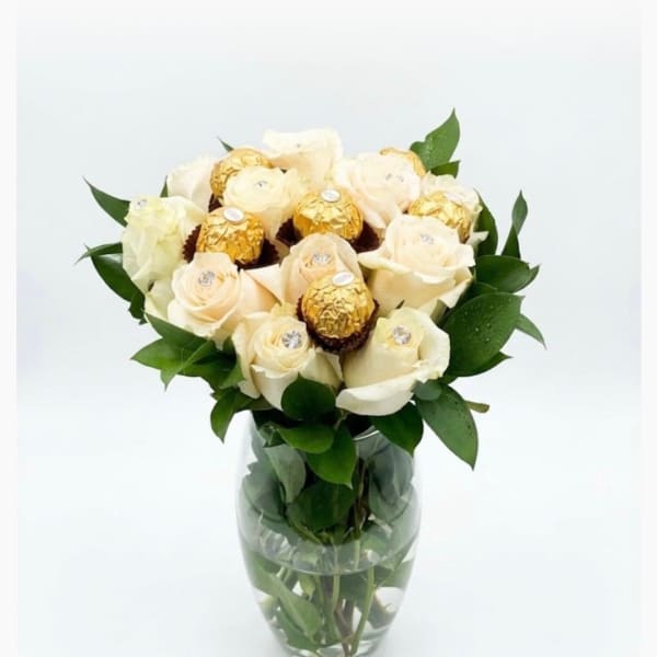 White roses with gold-wrapped chocolates in a glass vase