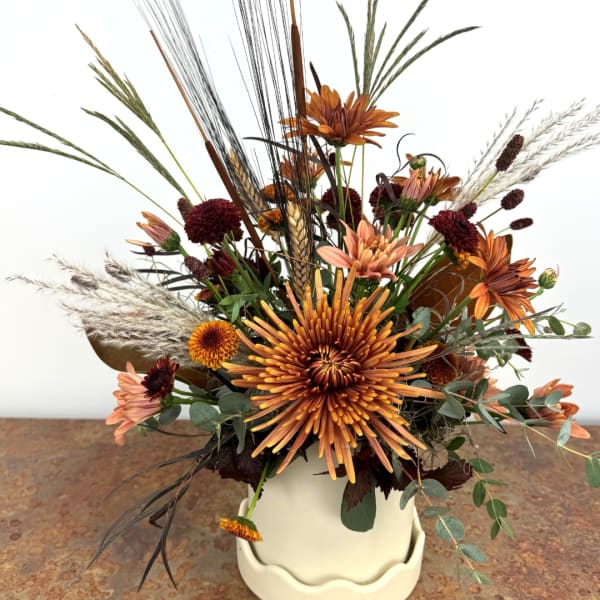 Autumn floral arrangement with orange and burgundy blooms in a white pot