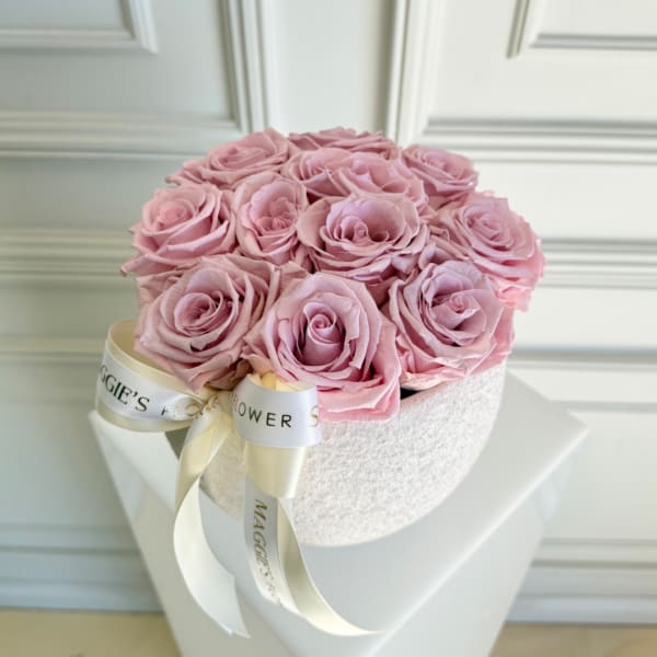 Pink roses arranged in a round white hat box with a ribbon bow