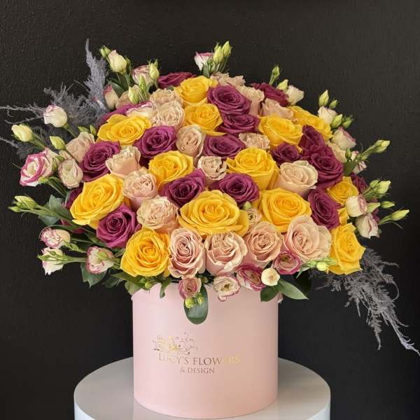 Large bouquet of yellow, blush, and purple roses in a pink hat box