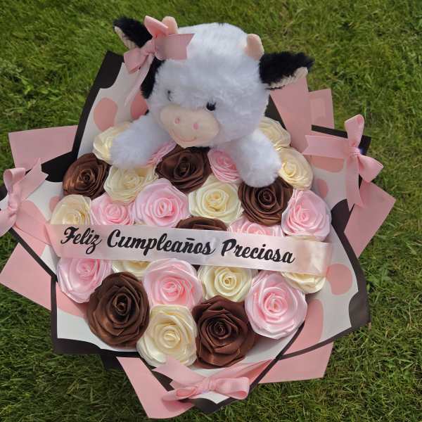 Plush cow on a bouquet of pink, cream, and brown roses with a birthday ribbon