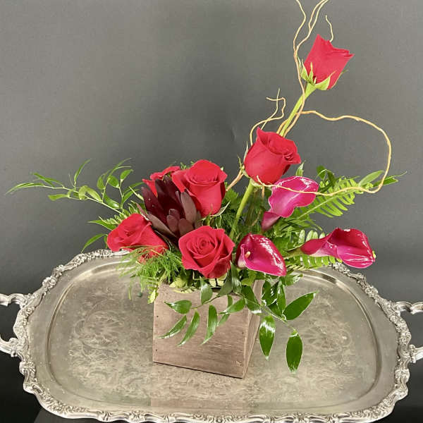 Red roses and pink calla lilies arranged in a square wooden vase