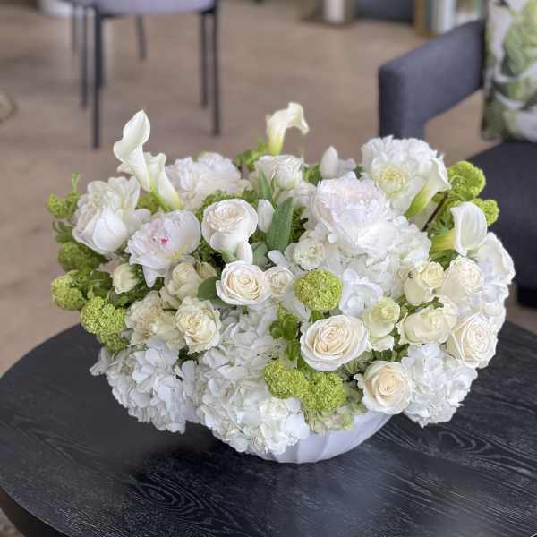White floral arrangement with roses, calla lilies, and green pom-pom blooms in a low vase