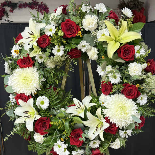 Large standing floral wreath with red roses, white lilies, and white daisies