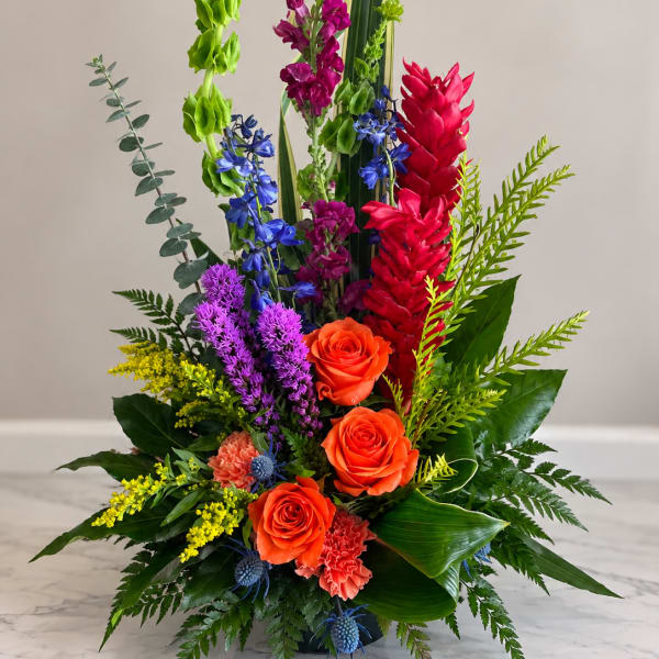 Tall multicolor floral arrangement with orange roses and bright tropical blooms