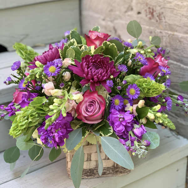 Mixed pink and purple flower arrangement in a woven basket