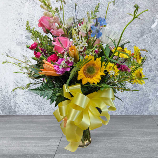 Mixed bouquet with sunflowers, pink roses, and a yellow ribbon in a glass vase