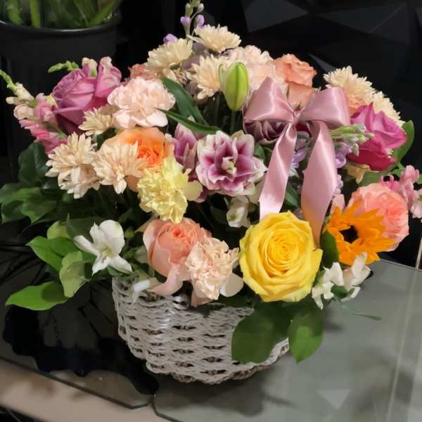 Mixed flower arrangement in a white wicker basket with a pink ribbon