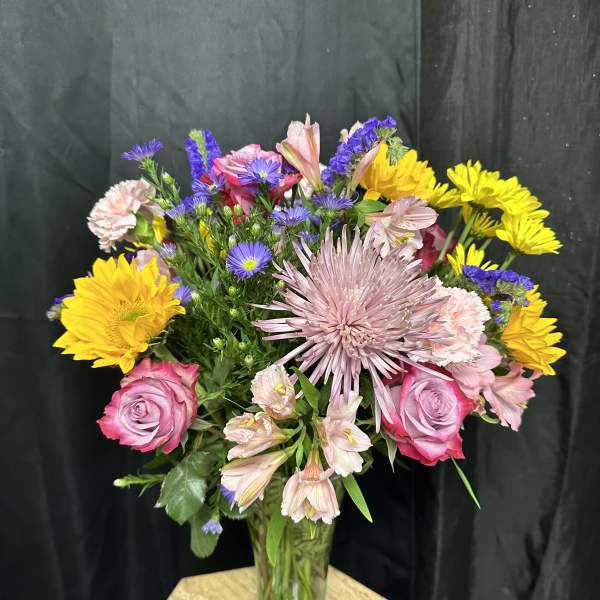 Mixed bouquet of pink, yellow, and purple flowers in a glass vase