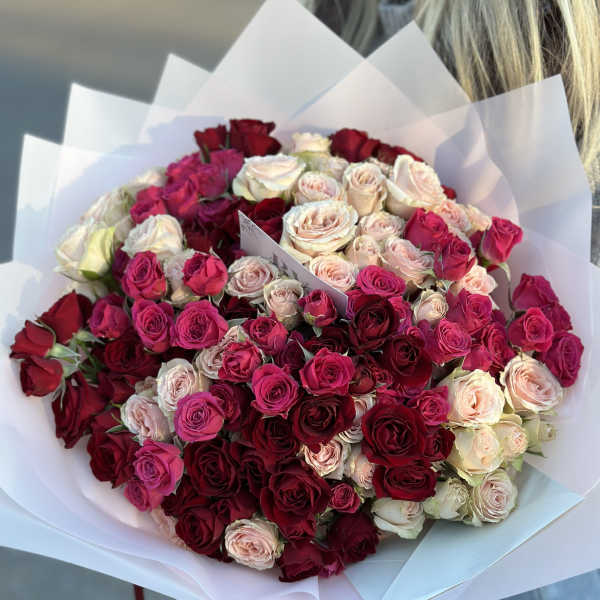 Large bouquet of red, pink, and blush roses wrapped in white paper