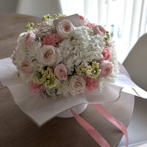 Round bouquet of pale pink and white flowers wrapped in paper