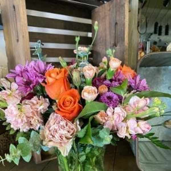 Mixed bouquet of orange, pink, and purple flowers in a glass vase