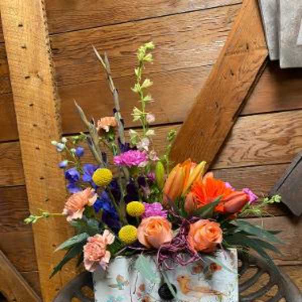 Mixed bouquet with orange roses and colorful blooms in a patterned box