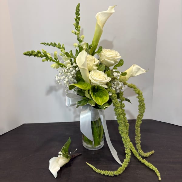 White calla lilies and roses in a glass vase with a matching boutonniere