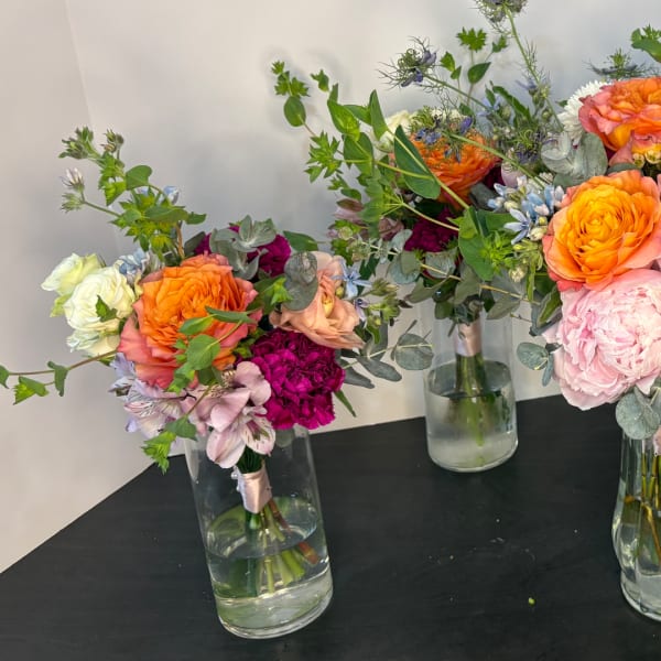 Three mixed floral bouquets in clear glass vases on a black table