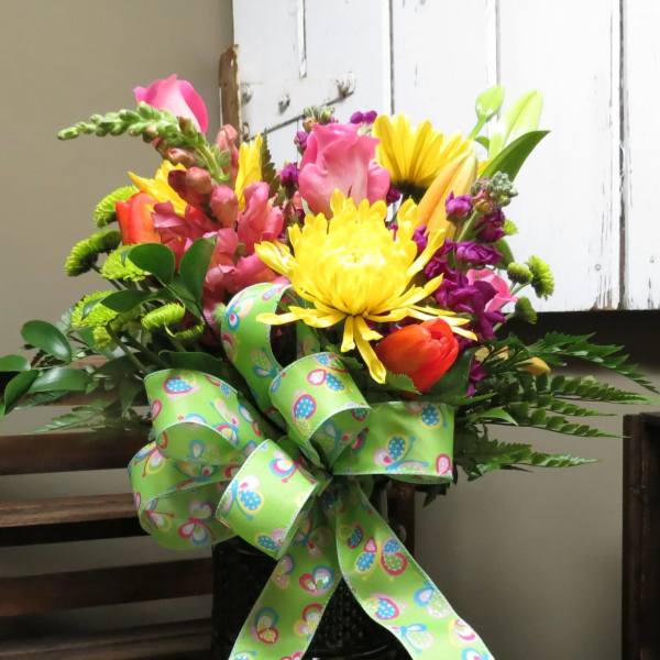 Colorful mixed flower bouquet in a black vase with a green patterned ribbon
