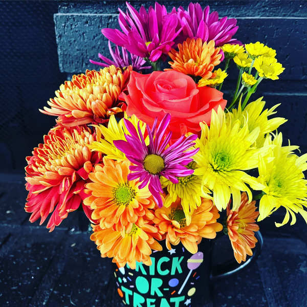 Colorful bouquet of daisies and a rose in a Halloween mug