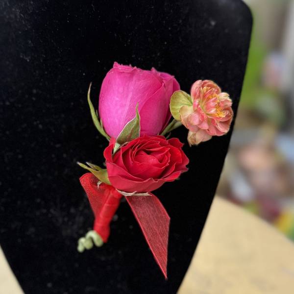 Pink and red rose boutonniere with a small peach flower on black fabric