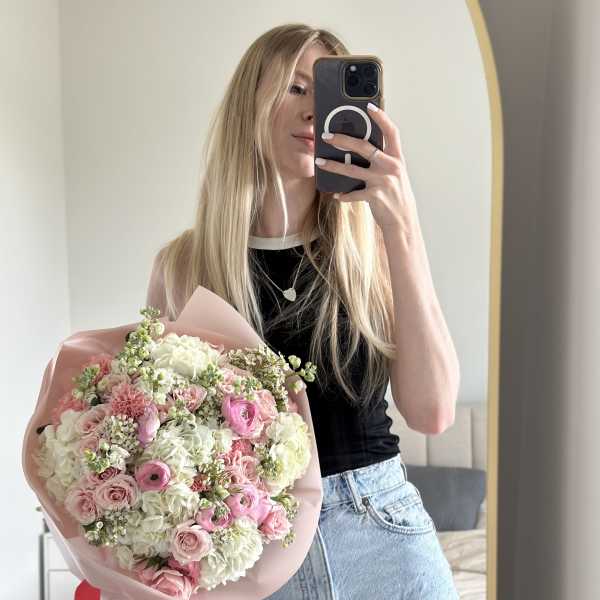 Woman holding a pink and white mixed flower bouquet in front of a mirror