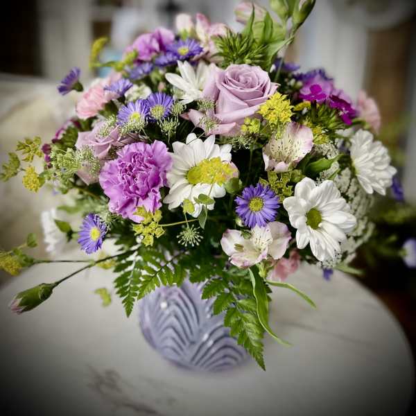 Mixed bouquet of pink, purple, and white flowers in a lavender vase