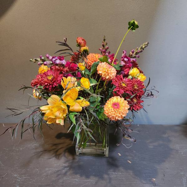 Mixed bouquet of yellow, pink, and orange flowers in a glass vase