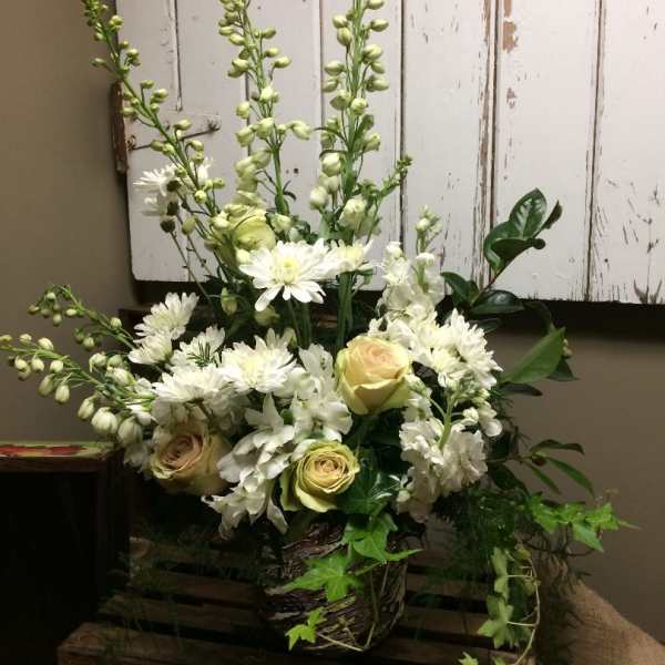 White floral arrangement with roses and tall spires in a rustic basket