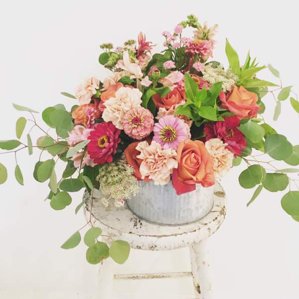 Mixed bouquet of pink, peach, and white flowers in a metal bucket