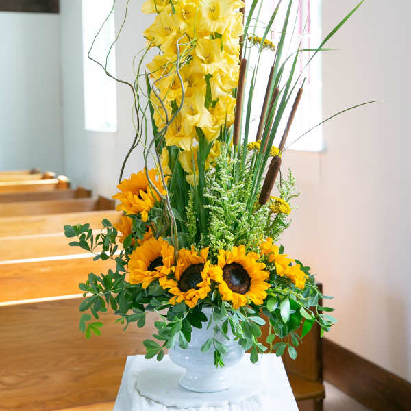 Tall yellow floral arrangement with sunflowers in a white pedestal vase
