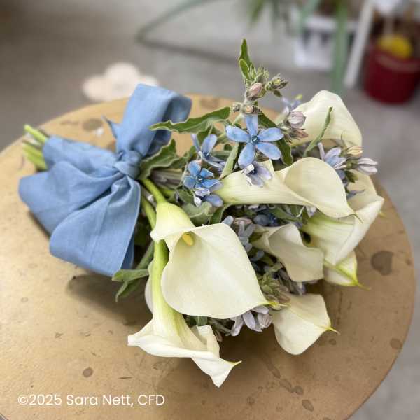Bouquet of white calla lilies and small blue flowers tied with a blue ribbon