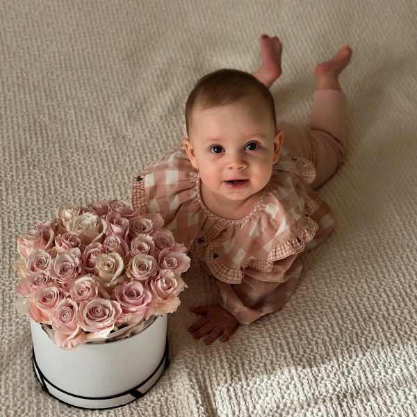Baby beside a box of pale pink roses on a carpet