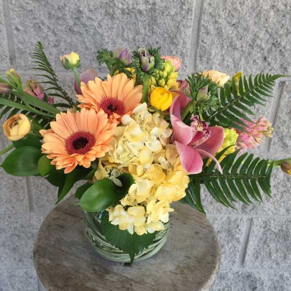 Mixed bouquet with peach gerberas, yellow hydrangea, and pink calla lilies in a glass vase