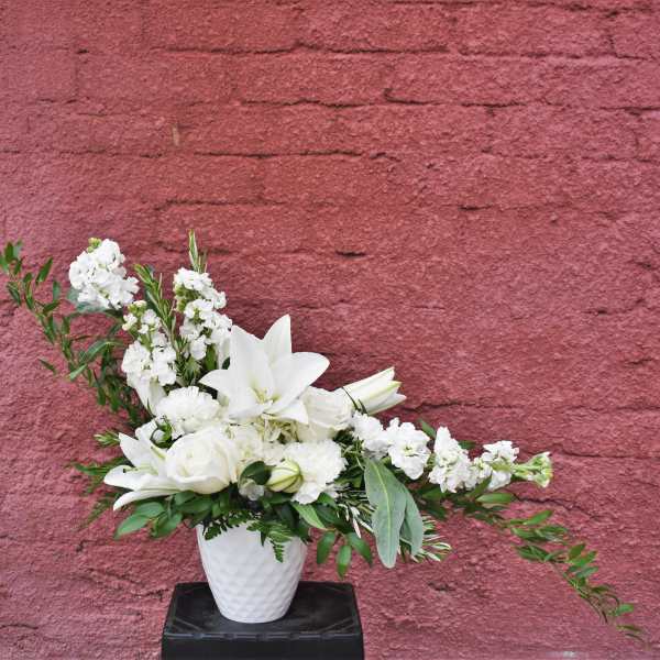 White floral arrangement in a white vase with lilies and roses