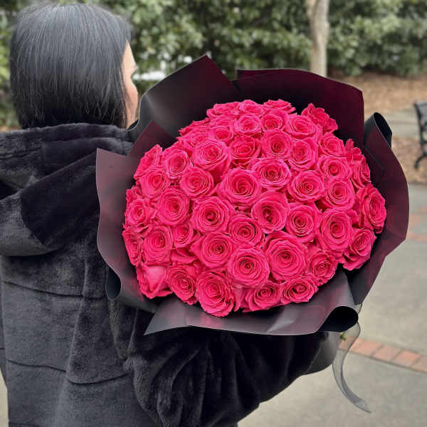 Person holding a large bouquet of bright pink roses wrapped in black paper