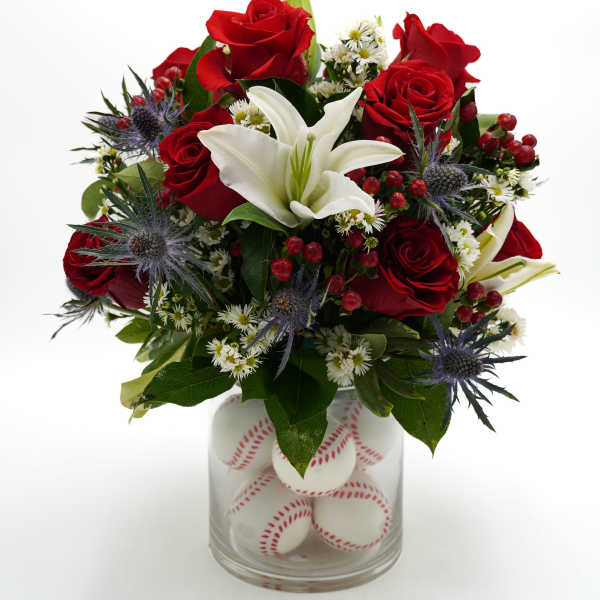Red roses and a white lily in a glass vase filled with baseballs