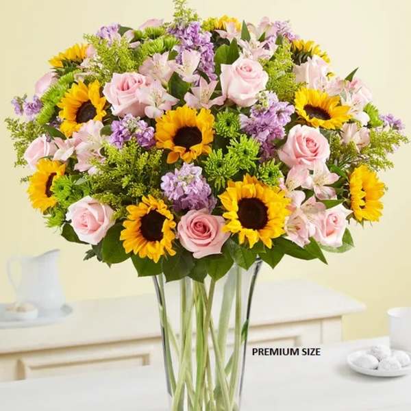 Bouquet of pink roses, sunflowers, and purple flowers in a clear glass vase