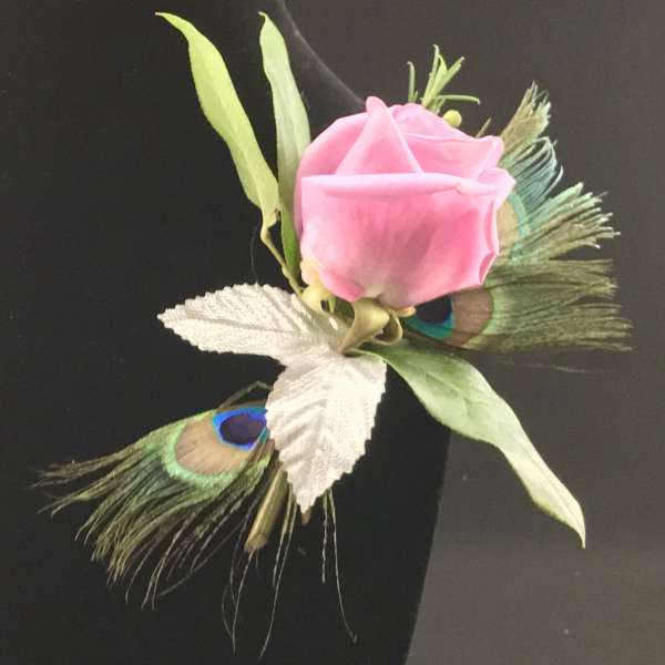 Pink rose boutonniere with peacock feathers and white leaves