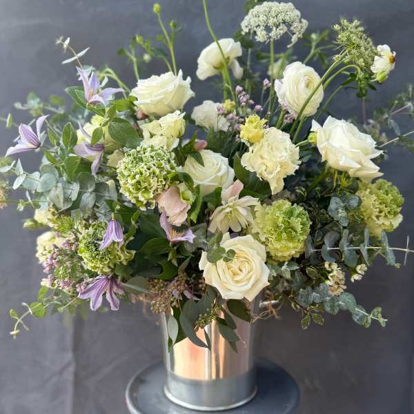 White roses and green blooms in a metal vase with purple flowers