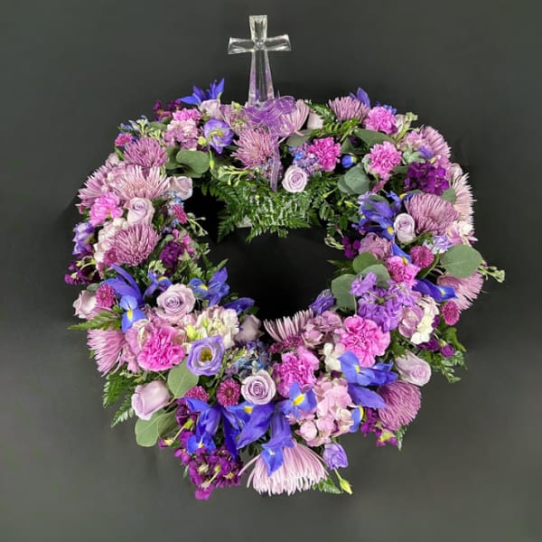 Circular wreath of purple and pink flowers with a clear cross topper