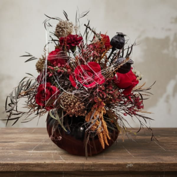 Red roses in a dark vase with dried accents and seed pods