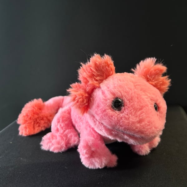 Pink plush toy animal with black eyes on a dark surface
