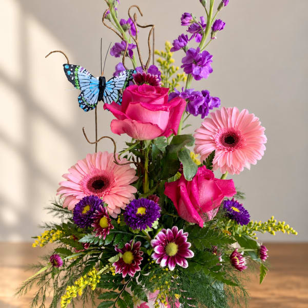 Pink roses and gerbera daisies in a butterfly-decorated vase with purple blooms